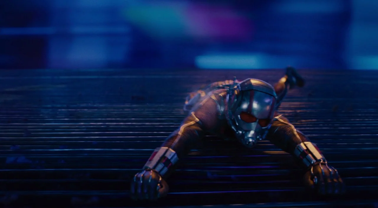 Ant-Man (2015) movie still: medium — A figure lies flat on a dark, ribbed metallic surface under a blue hue. The masked character stretches their…
