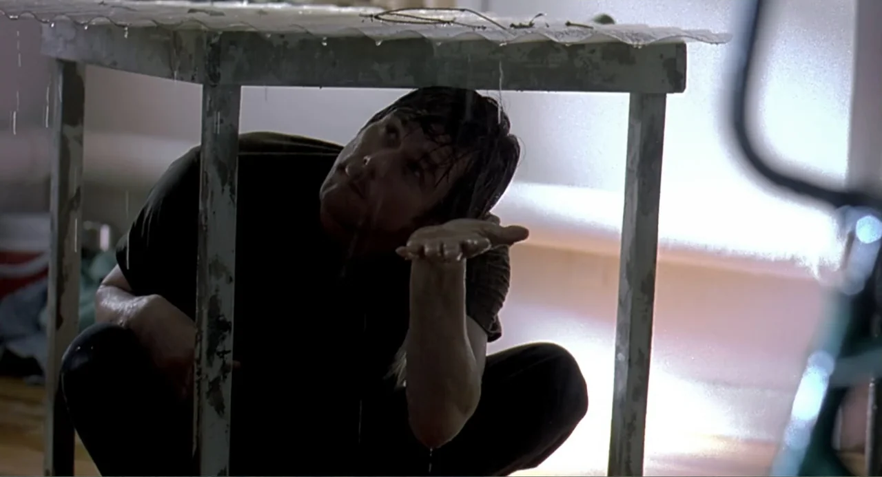 Eternal Sunshine of the Spotless Mind (2004) movie still: medium — A man crouches beneath a metal table in an interior space with leaking water. He…