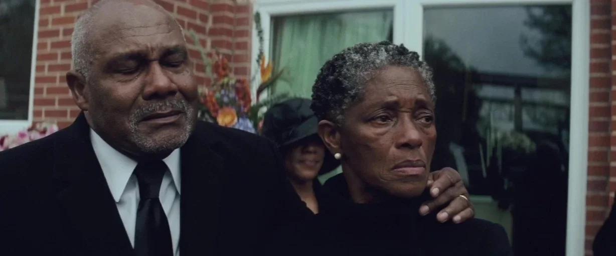 Queen & Slim (2019) movie still: medium — An older couple stands outdoors in front of a red brick wall. The man rests his hand on the woman's…