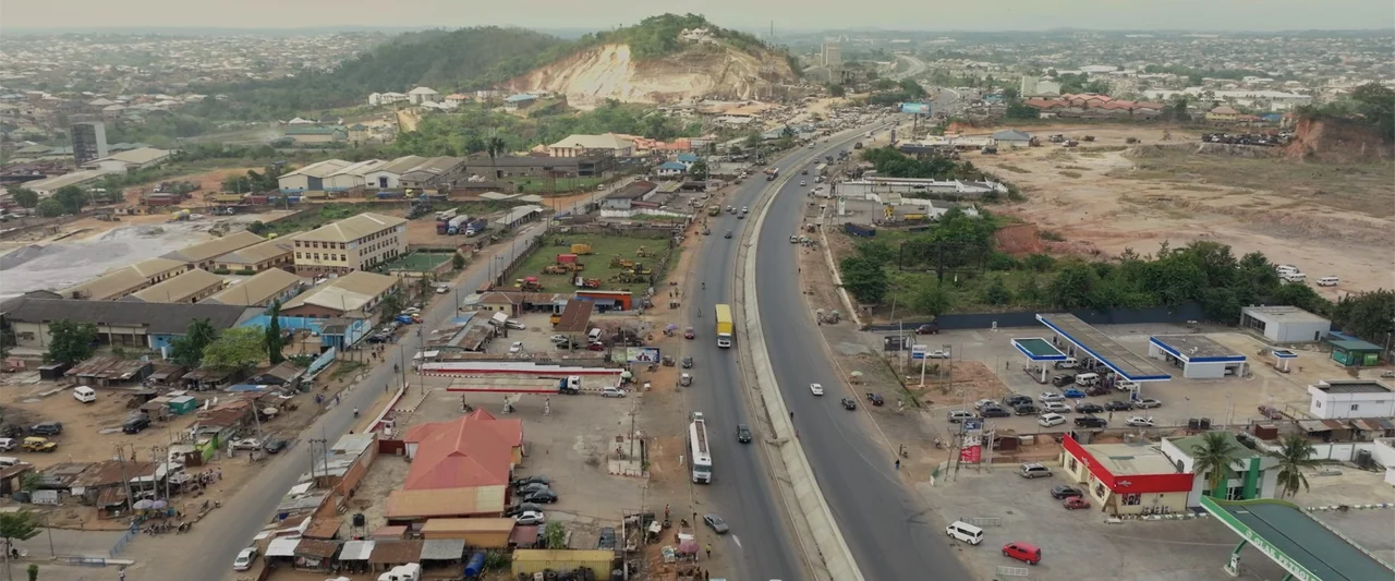 Big Love (2012) movie still: establishing — A high-angle view of a sprawling highway infrastructure passing through a developing urban area.…