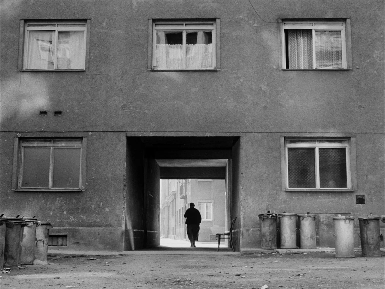 The Sun In A Net (1963) movie still: wide — A grey concrete residential building features a dark central passageway and multiple windows. An older…
