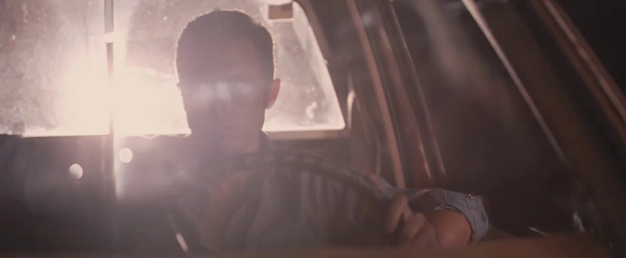 Ain’t Them Bodies Saints (2013) movie still: medium — A man drives a car at night with intense light blindingly hitting the windshield. The cabin…