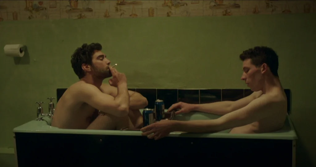 God’s Own Country (2017) movie still: medium — A dimly lit bathroom features green walls and vintage patterned wallpaper above the tub. Two…