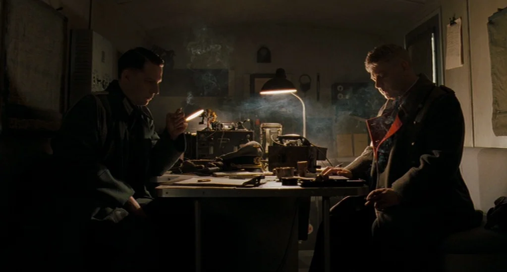 Valkyrie (2008) movie still: medium — A cramped military office space contains desks, radio equipment, and cigarette smoke. Two men in uniform…