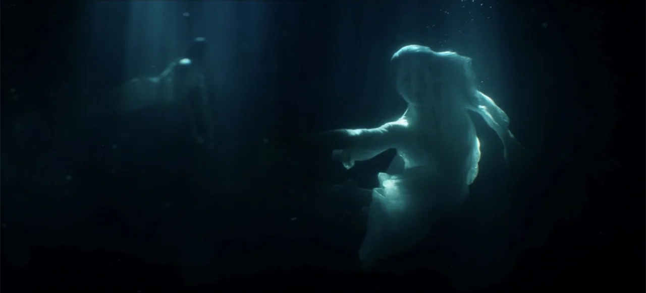 I Still See You (2018) movie still: medium — Two figures are submerged in dark, deep water under a focused beam of light. A woman in a light garment…