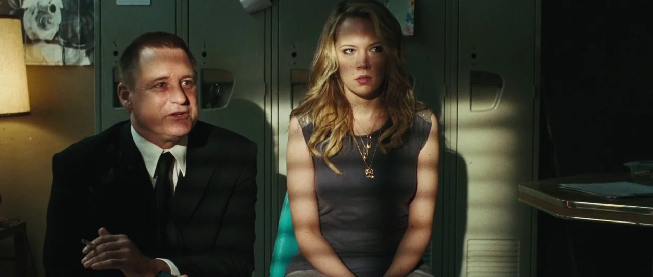 Surveillance (2008) movie still: medium — A dimly lit room features rows of metal lockers in the background. A man and a woman sit together in front…