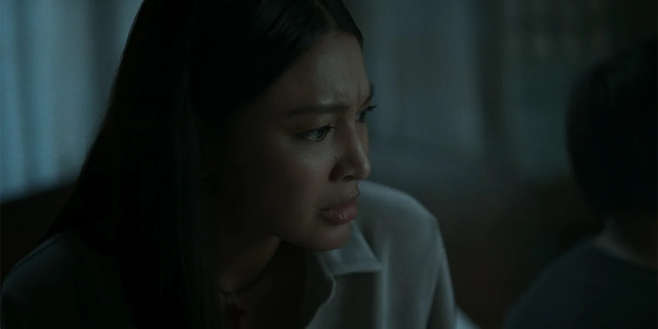 Nokturno (2024) movie still: closeup — A dimly lit room interior contains a woman looking away from the camera. The subject has a concerned…