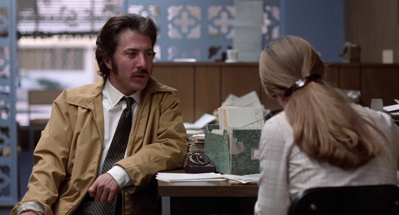 Straight Time (1978) movie still: medium — A 1970s office interior features wood paneling, a green file box, and metal partitions. A man in a tan…