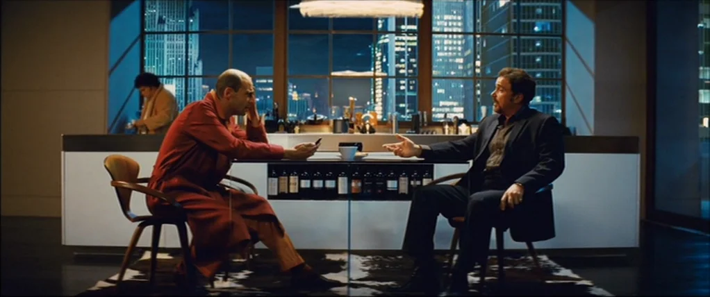 Kick Ass (2010) movie still: wide — A luxury apartment interior features a glass table and a view of night skyscrapers. Two men sit opposite each…