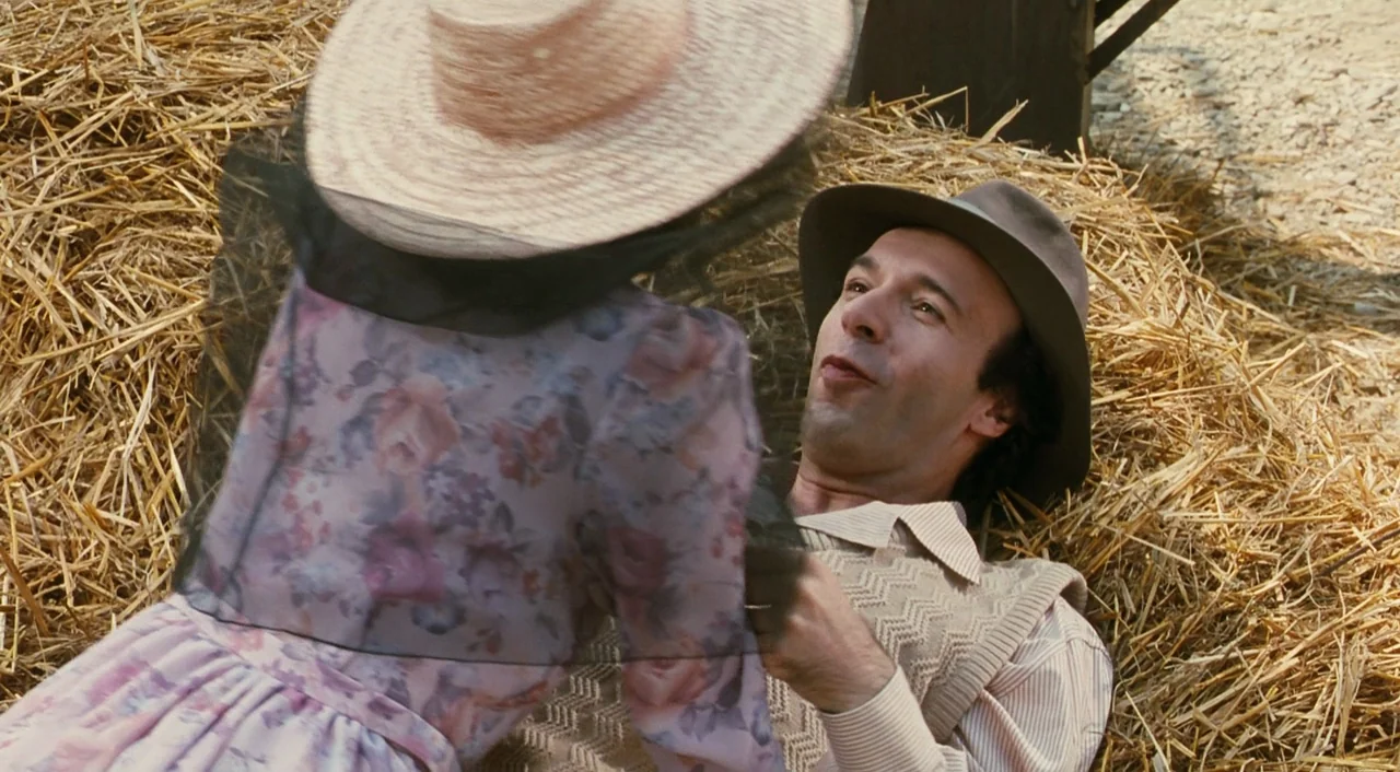 Life is Beautiful (1997) movie still: medium — A man lies on a pile of loose golden straw in an outdoor area. A woman wearing a straw hat and floral…
