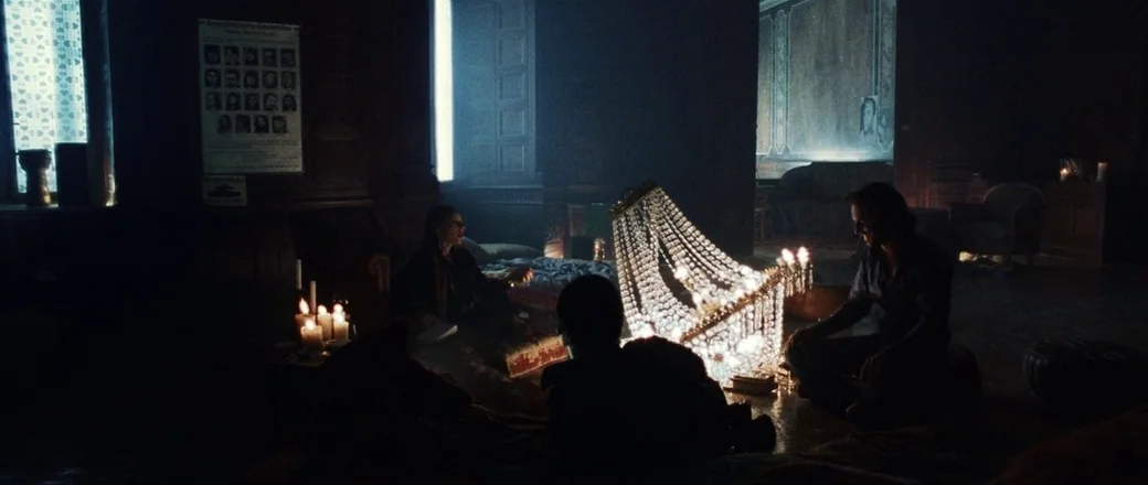 Munich (2005) movie still: wide — A dark, wood-paneled room contains a fallen crystal chandelier providing bright local illumination. A man, a…