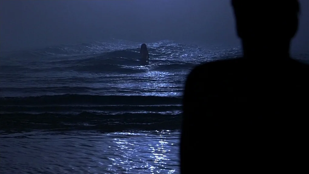 Ask The Dust (2006) movie still: wide — A dark night scene at the water edge with a vast ocean horizon. A shadowy figure stands in the surf facing a…