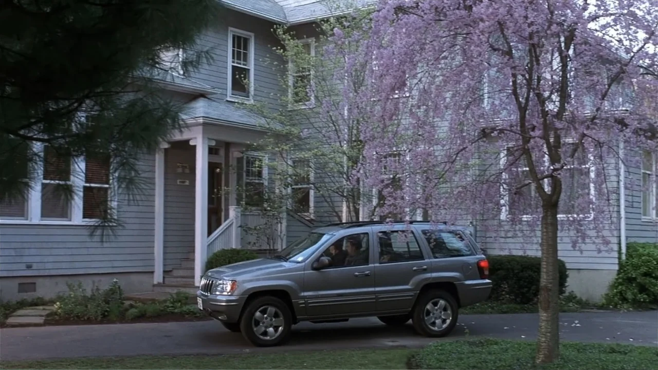 Analyze That (2002) movie still: wide — A grey two-story house with blue horizontal siding sits behind a paved driveway. An suv with a driver moves…