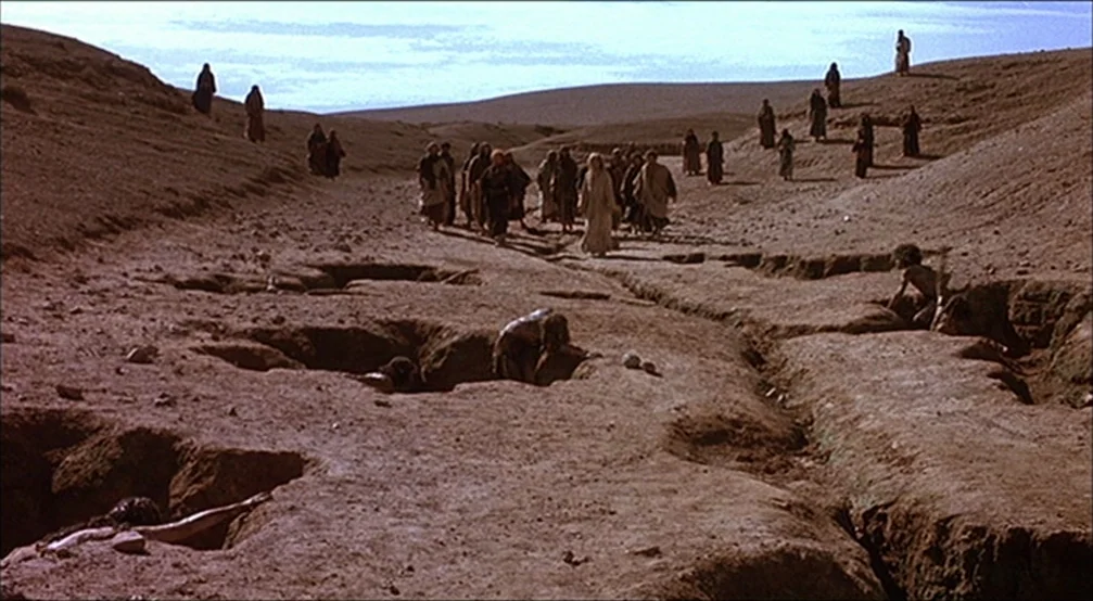 The Last Temptation Of Christ (1988) movie still: wide — A dry, undulating desert landscape is characterized by uneven, cracked earth and deep pits.…