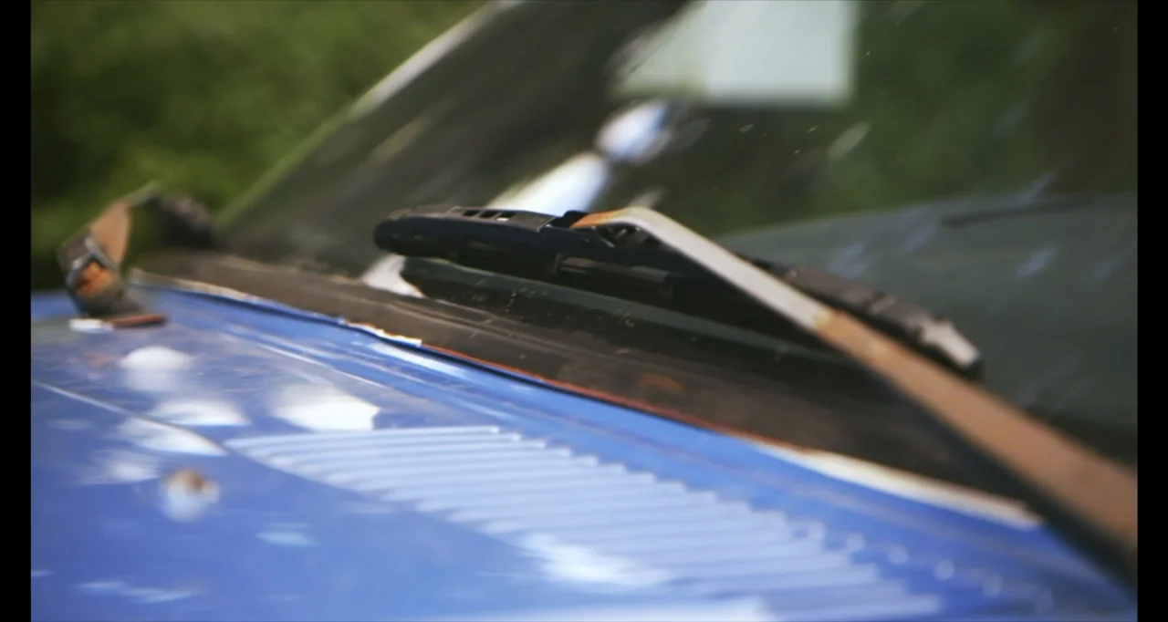 Hunted by My Husband: The Untold Story of the DC Sniper (2025) movie still: closeup — A close view of a blue car hood and the base of the…