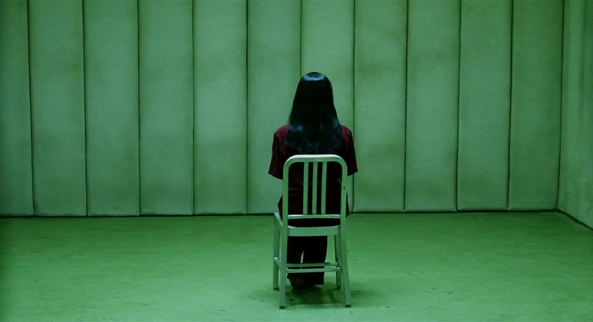 Hellboy (2004) movie still: fullbody — A windowless room features walls lined with green vertical padding and a green floor. A woman with long dark…