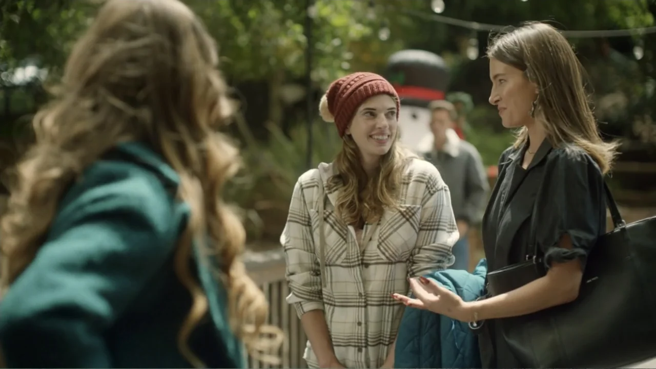 A Carpenter Christmas Romance (2024) movie still: medium — Three young women gather for a conversation in a brightly lit outdoor park setting. The…