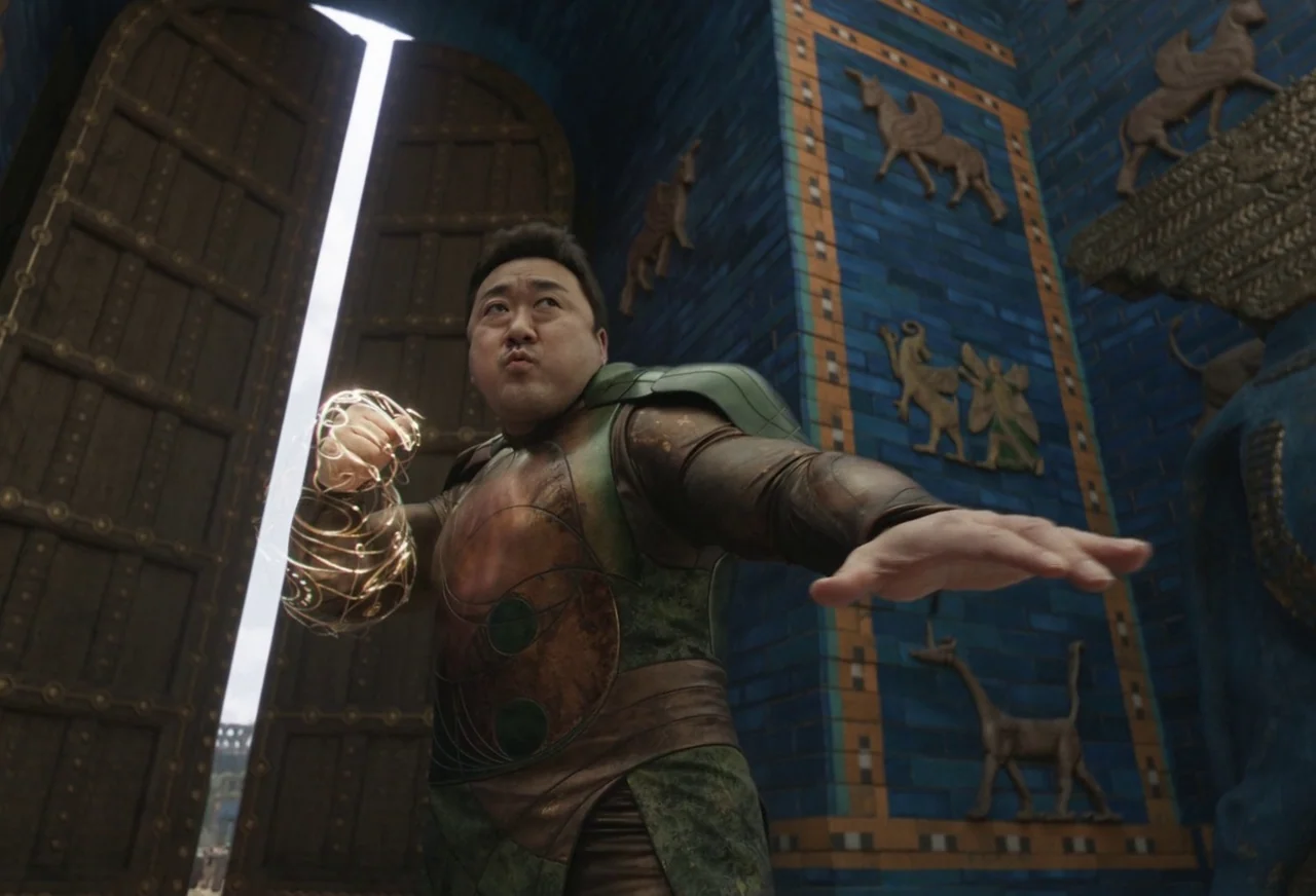 Eternals (2021) movie still: medium — A man stands before a monumental blue-tiled gate adorned with ancient mythological animal reliefs. He strikes…