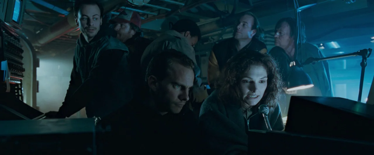 The Abyss (1989) movie still: medium — A cluttered, dimly lit submarine control room filled with wires and electronics. A group of people monitor…