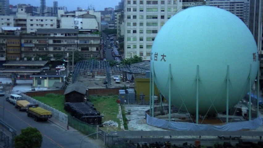 The Terrorizers (1986) movie still: establishing — An urban industrial landscape features a large, pale turquoise spherical gas storage tank.…