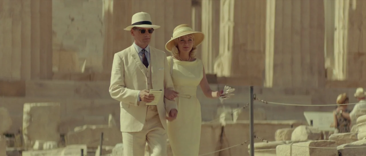 The Two Faces of January (2014) movie still: fullbody — A man and woman walk together past large, weathered stone columns of an ancient ruin. The…