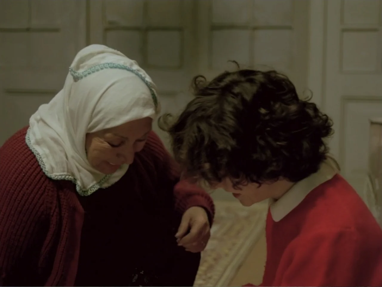 Don't Let Them Shoot the Kite (1989) movie still: medium — An interior space features an elderly woman and a child close together indoors. The two…