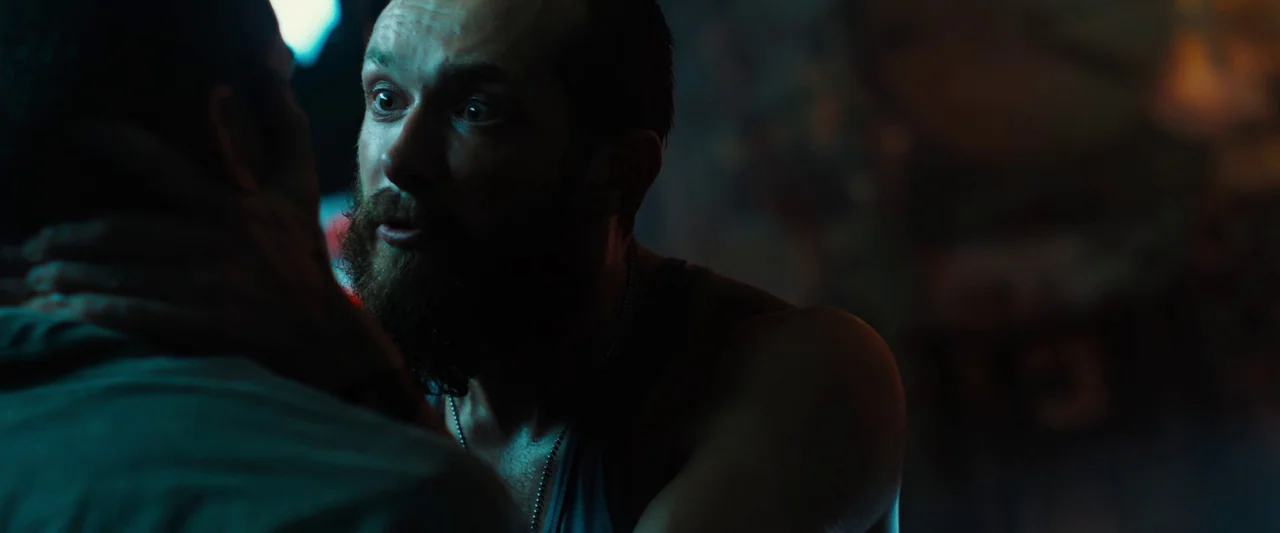 Black Sea (2014) movie still: closeup — A dimly lit interior space with dark, indistinct surroundings and blue rim lighting. A bearded man with a…