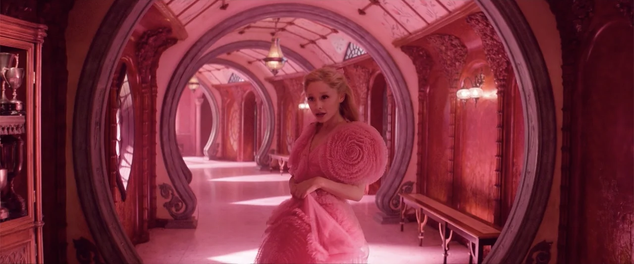Wicked (1998) movie still: medium — A long interior hallway features arched doorways and pink monochromatic walls. A woman stands in the center…