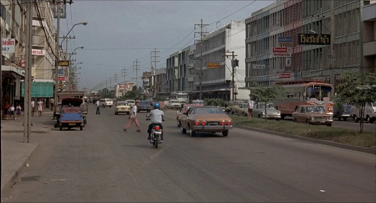 The Man With the Golden Gun (1974) movie still: wide — An urban street scene in a Southeast Asian city features multi-story buildings and traffic. A…