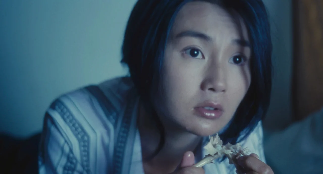 Comrades: Almost A Love Story (1996) movie still: closeup — A close view of a woman illuminated by cold light in a dark room. She holds a small…