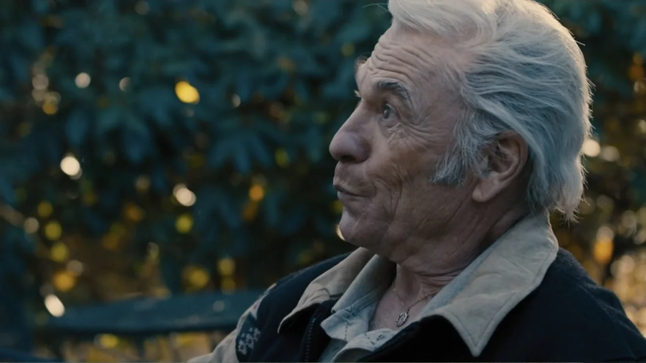 Bleed for This (2016) movie still: closeup — An elderly man with silver hair sits outside during the golden hour. He is looking off to the side with…