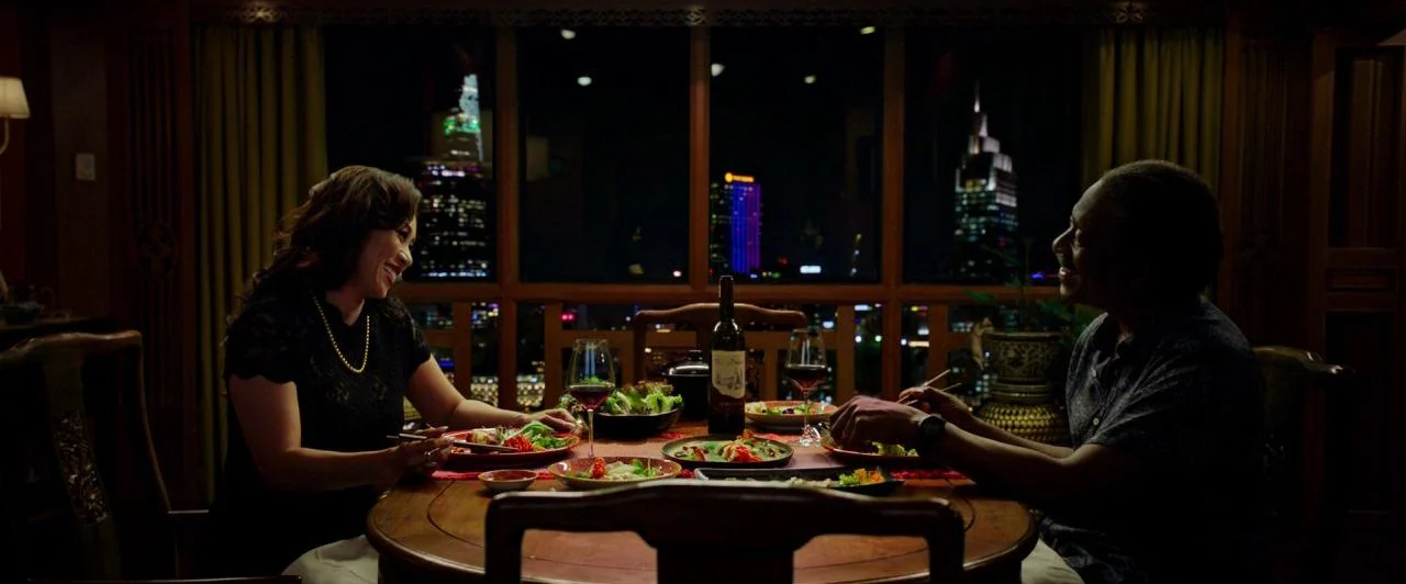 Da 5 Bloods (2020) movie still: medium — An interior dining area features a round wooden table set against a large window. A man and woman sit…