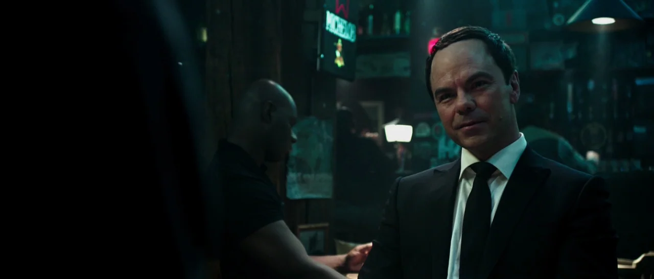 Deadpool (2016) movie still: medium — A dimly lit bar interior features wooden architectural elements and a visible neon signage. A man in a suit…
