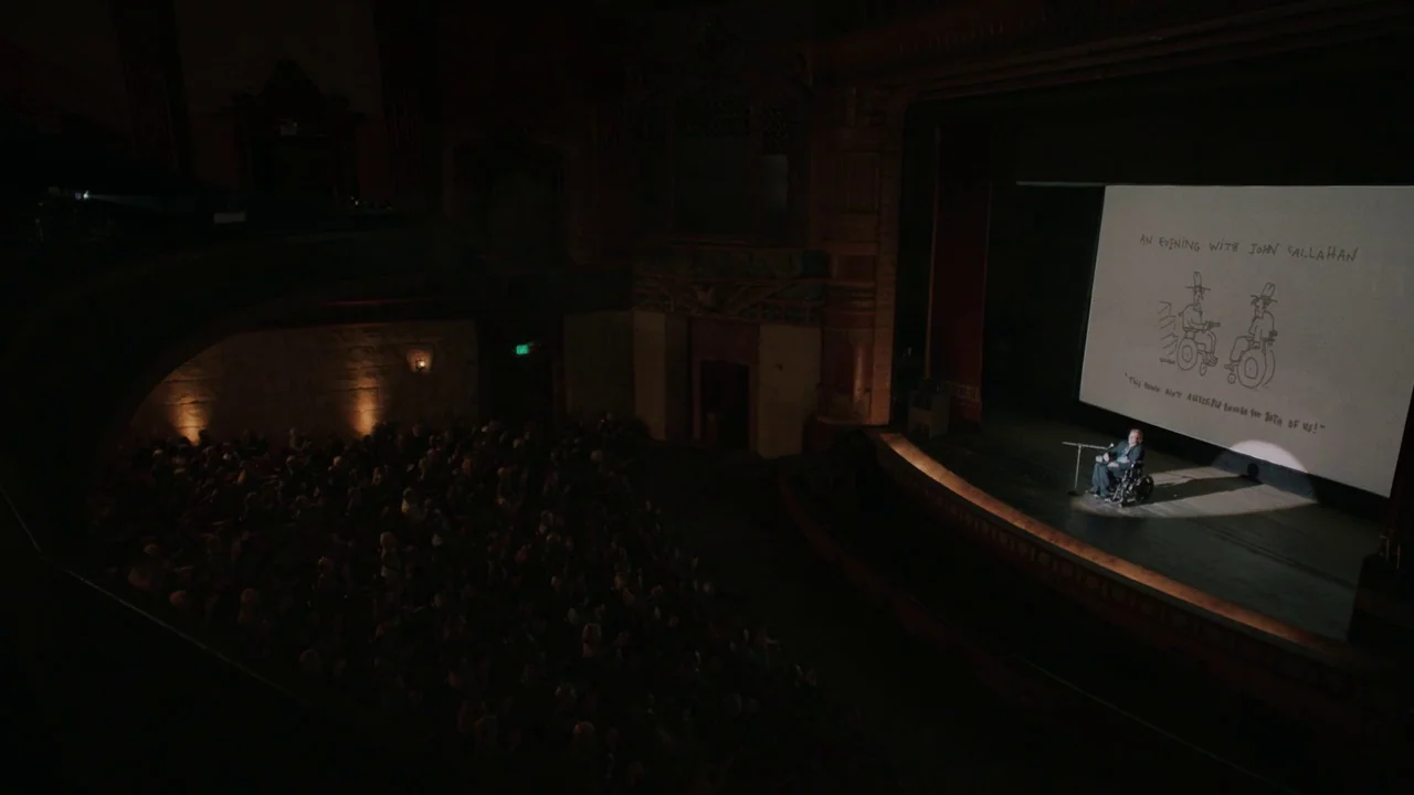 Don't Worry, He Won't Get Far on Foot (2018) movie still: wide — A large, dark vintage theater interior with a crowded audience sitting in the…