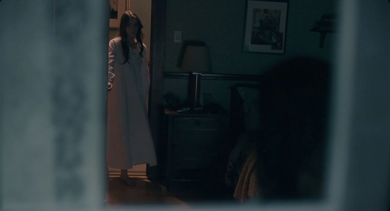 The Moth Diaries (2011) movie still: wide — A dimly lit room seen from the perspective of someone sitting on a bed. A young woman stands in the open…
