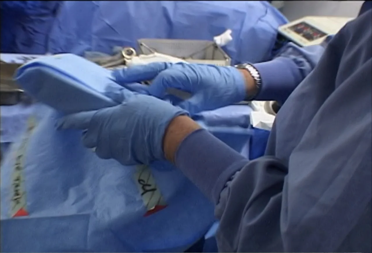 Plastic Disasters (2006) movie still: closeup — An operating room setup features blue sterile drapes covering medical equipment and surfaces. Gloved…