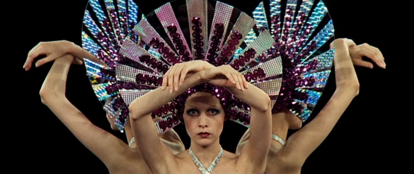 The Boy Friend (1971) movie still: medium — A dark, empty void serves as the background for a performer. A woman wears an elaborate purple sequined…
