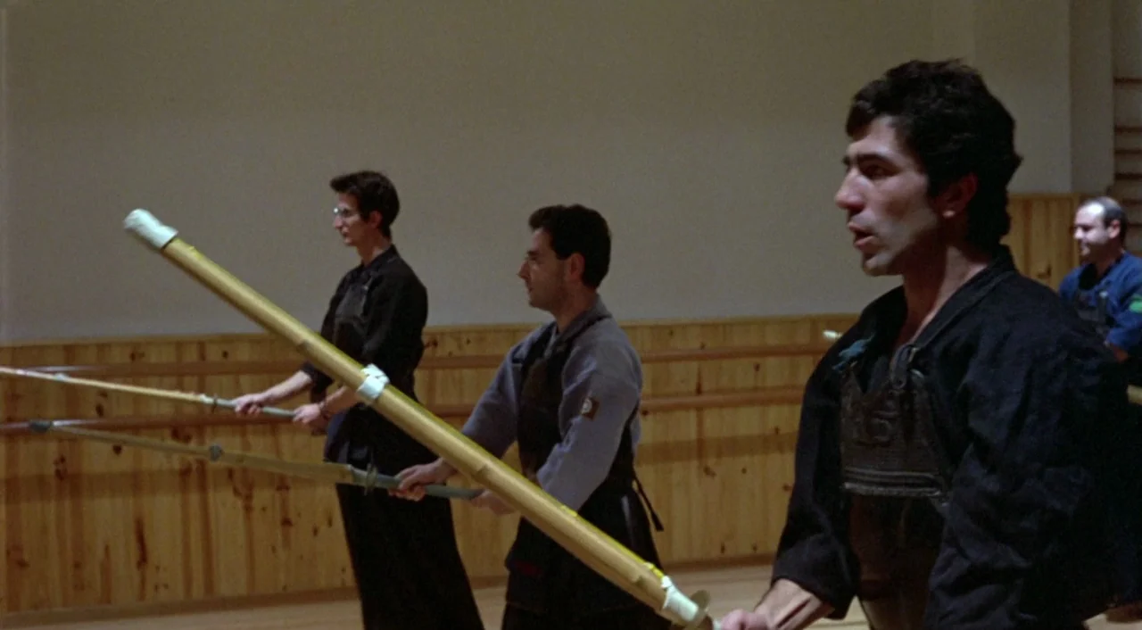 What Have I Done To Deserve This? (1984) movie still: medium — A wooden-walled practice hall with pale mats and horizontal rail fixtures. Several…