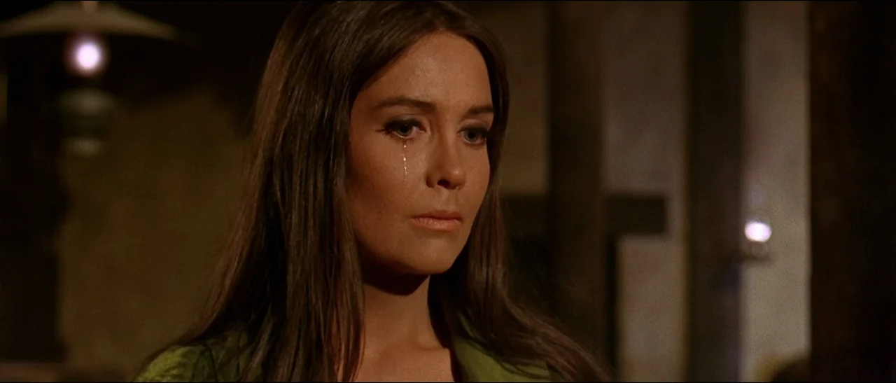 The Appaloosa (1966) movie still: closeup — The background consists of a dark, unfocused interior with a single glowing light source. A woman with…