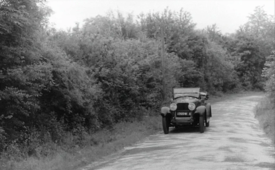 Judex (1966) movie still: wide — A vintage open-top automobile is parked on an unpaved narrow country road. Thick foliage and dense trees line both…