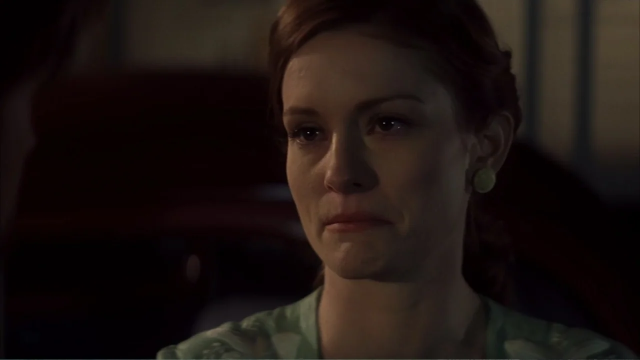The Notebook (2004) movie still: closeup — A dimly lit indoor space with blurred dark forms visible in the background. A woman with red hair looks…