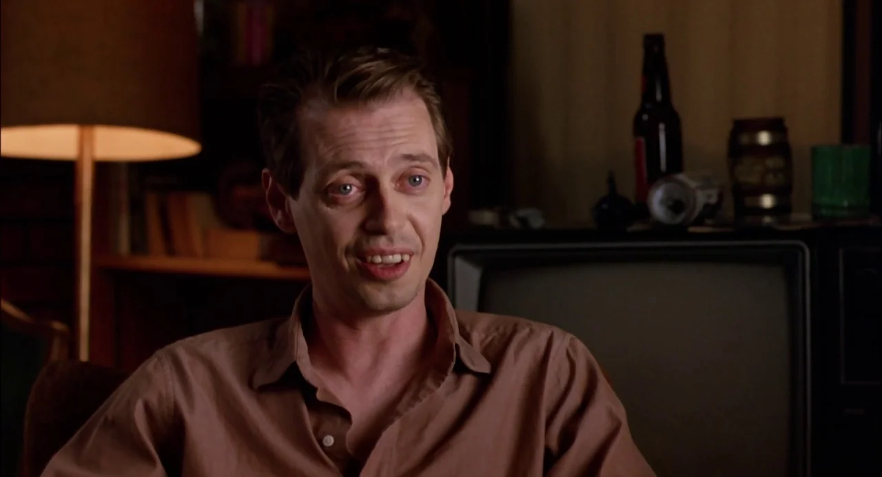 Trees Lounge (1996) movie still: closeup — A man sits in a dimly lit room with a television and lamp behind him. The man speaks directly toward…