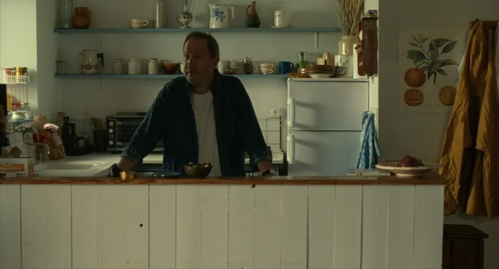 Things to Come (2016) movie still: medium — A home kitchen features white paneled cabinetry, open shelves filled with dishes, and a refrigerator. A…