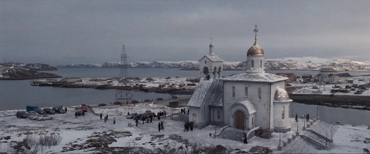 Leviathan (2014) movie still: establishing — A white Orthodox church stands on a snowy, desolate coast overlooking a frozen bay. People in winter…