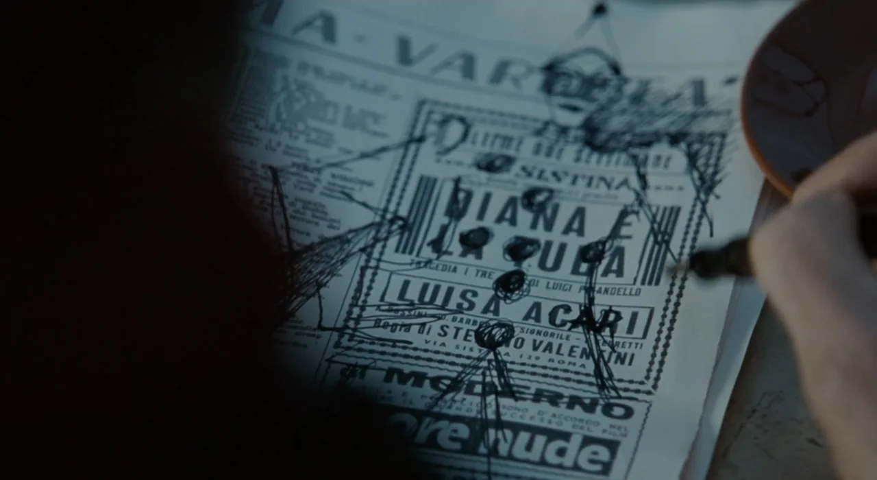 The Great Beauty (2013) movie still: closeup — A close-up view shows a person's hand marking up a vintage newspaper clipping. The printed paper…
