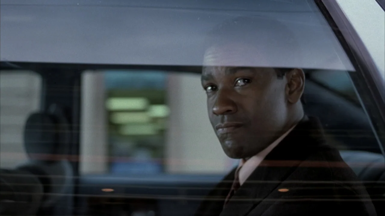 John Q (2002) movie still: closeup — A man sits inside the back seat of a dark vehicle at night. He turns his head to look through the glass as…