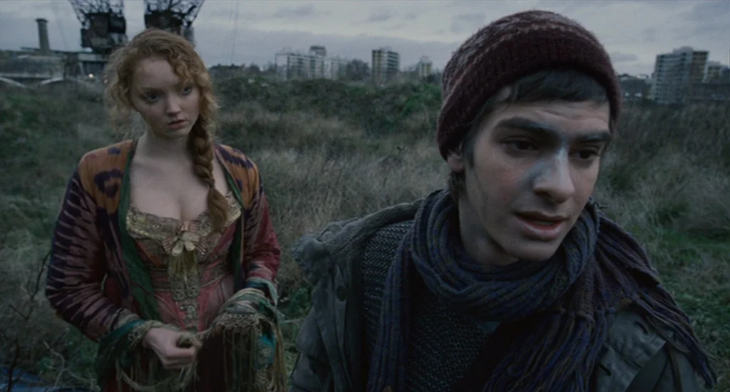 The Imaginarium of Doctor Parnassus (2009) movie still: medium — An open field with dried grass stretches toward distant city apartment buildings. A…