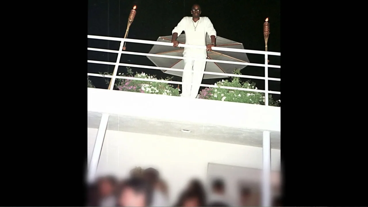 Diddy: The Making of a Bad Boy (2025) movie still: fullbody — An outdoor night scene shows a man standing on a white balcony with railings. The…