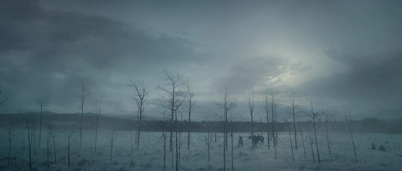 The Revenant (2015) movie still: wide — A vast, flat snowy clearing is dotted with thin, leafless trees under a grey sky. Two figures on horseback…