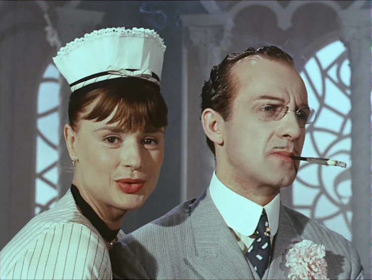 All These Women (1964) movie still: medium — Two individuals stand in an interior space with large arched decorative windows behind them. A woman in…